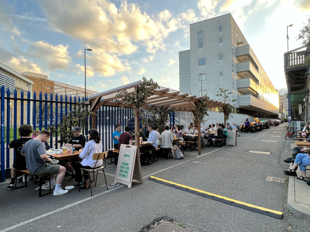 People sitting at benches outside a Villages Brewery in Deptford, London, at sunset
