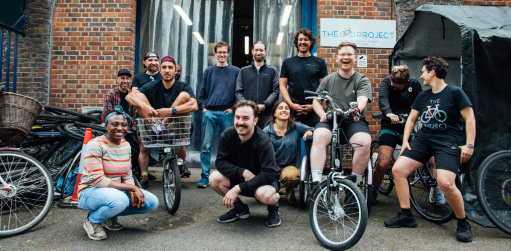 The Bike Project team stands in front of the workshop smiling at the camera.