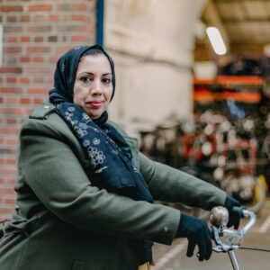 A refugee woman proudly posing on her bike in front of The Bike Project workshop