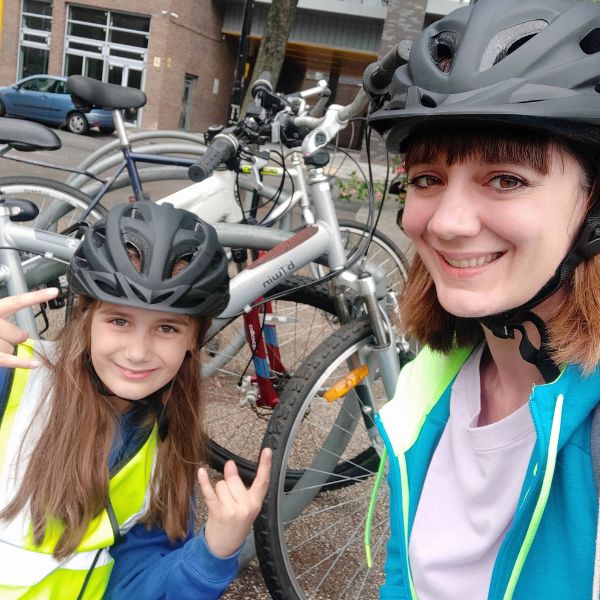 A woman and her daughter smiling with their bikes, with the daughter doing a 'rock on' hand motion