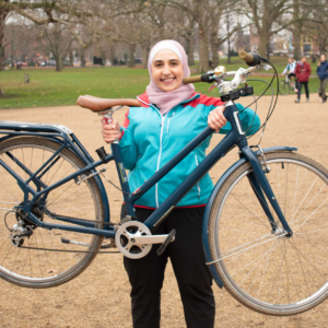 A refugee woman in a colourful outfit proudly holding up her bike